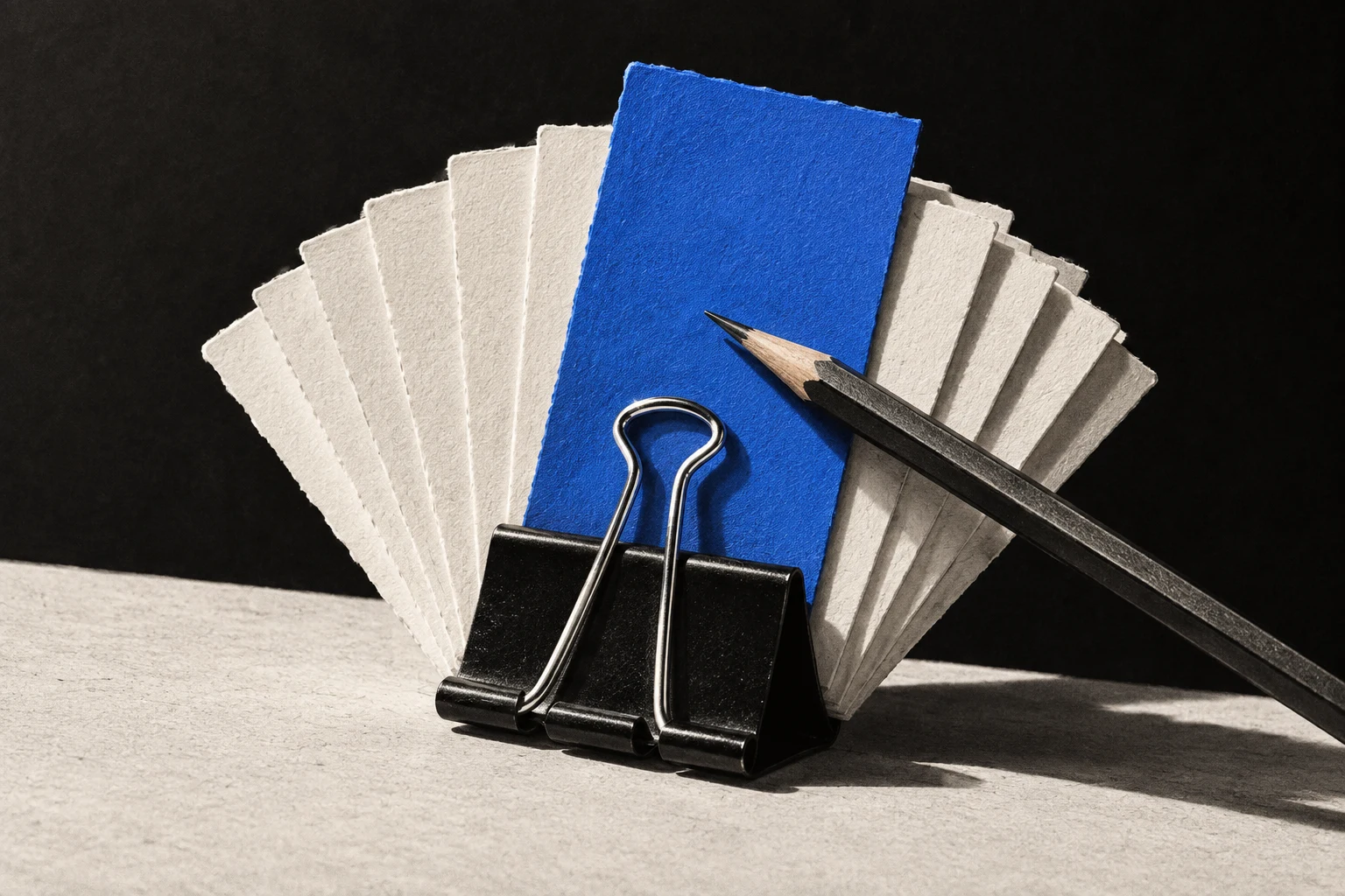 One blue card stands above a fan of ivory cards held together by a binder clip.